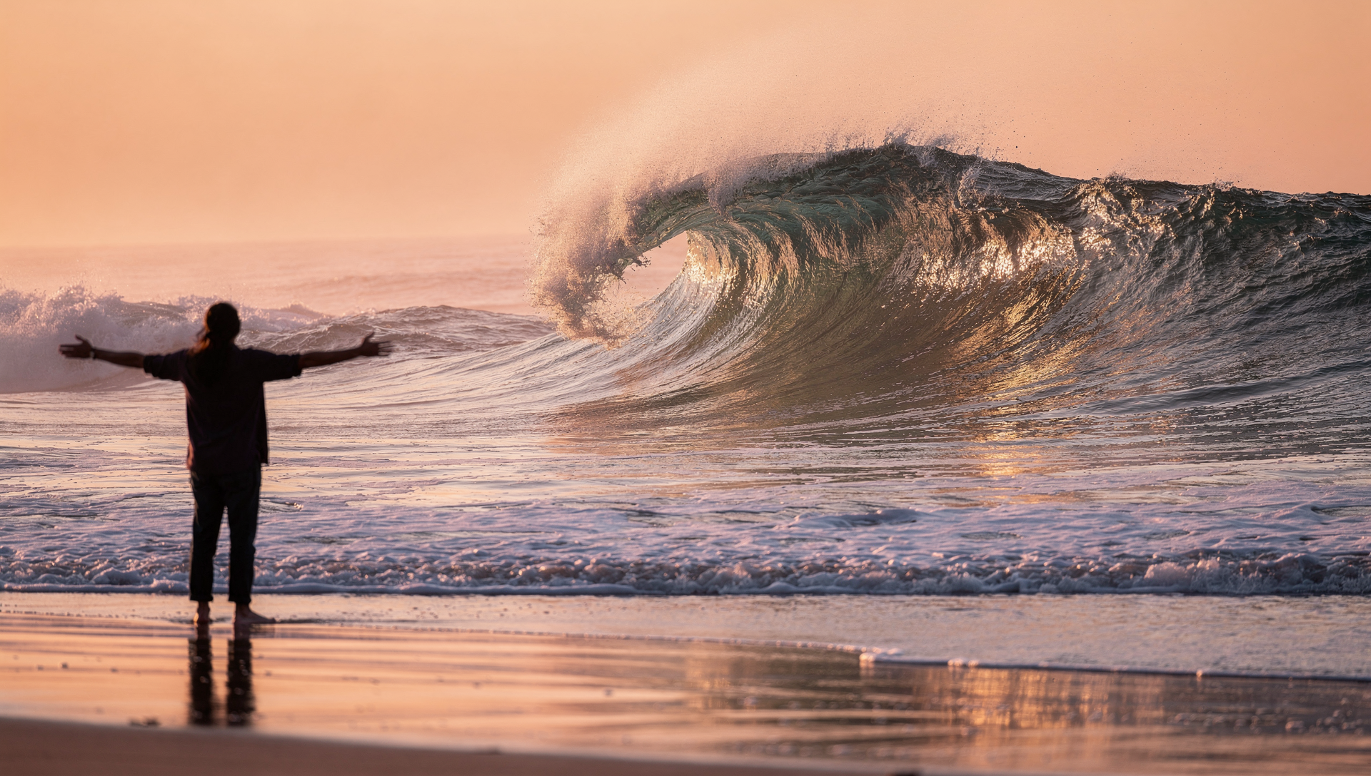 Silueta de una persona con los brazos abiertos frente a una gran ola rompiendo en la playa durante el atardecer, simbolizando la aceptación y la entrega consciente.